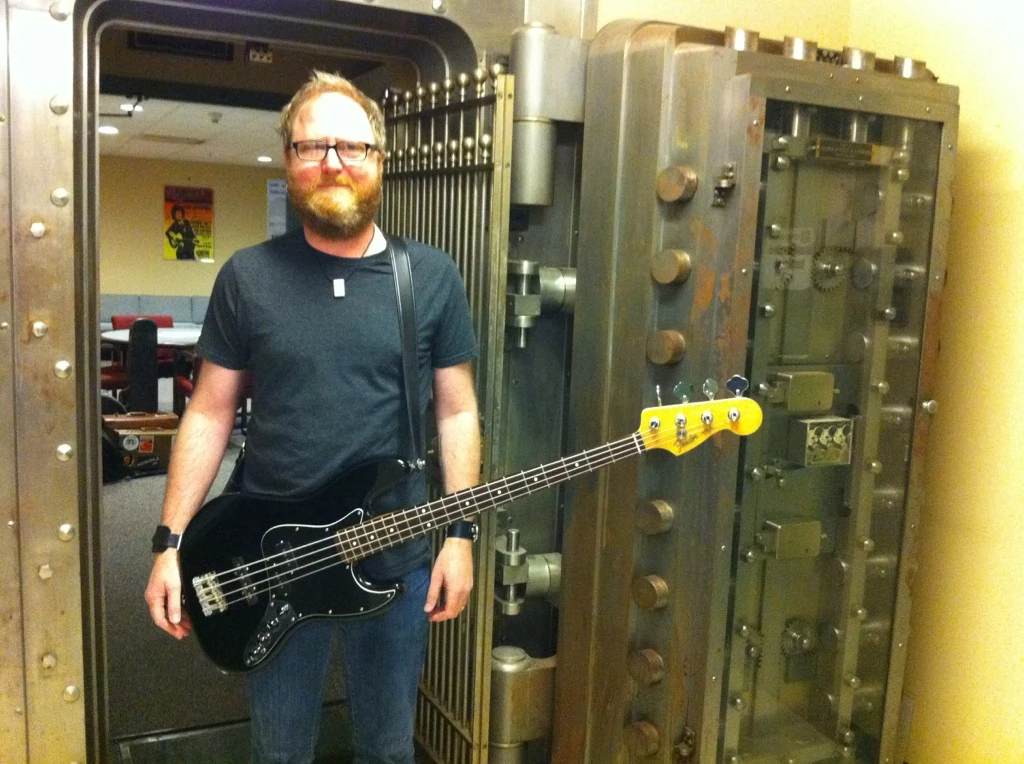 Eric Jarvis holding a bass guitar beside a large bank vault